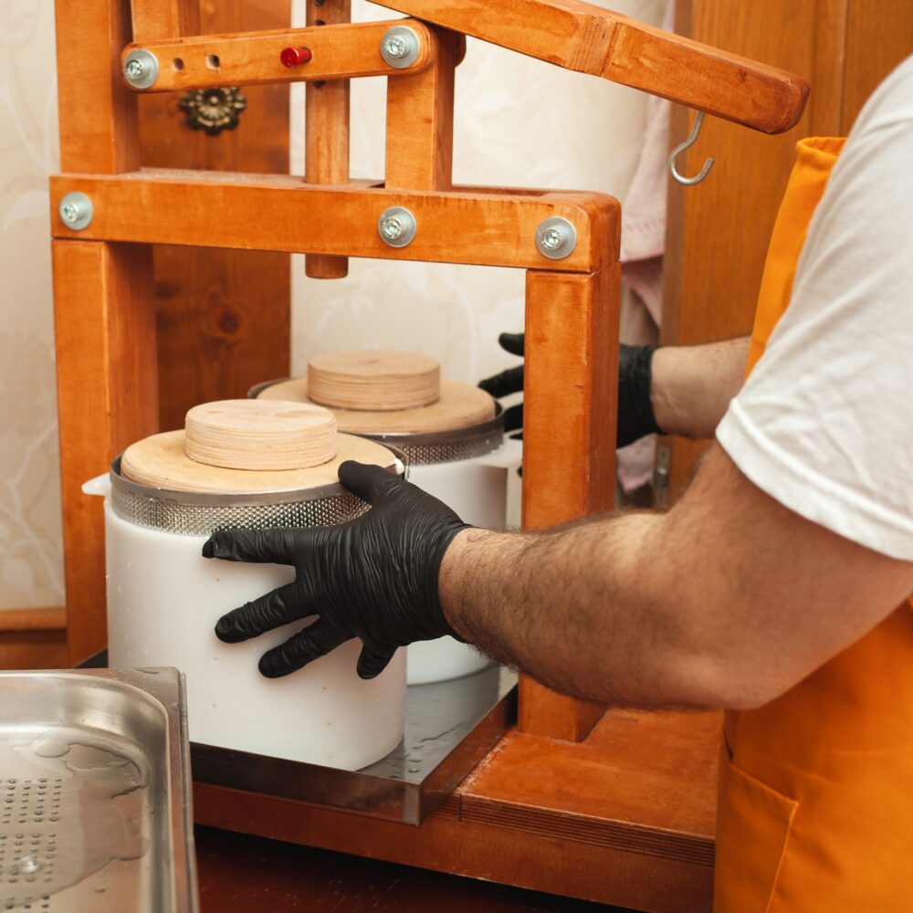 cheesemaker puts cheese under press, whey. Home production, business, portrait. Wooden equipment