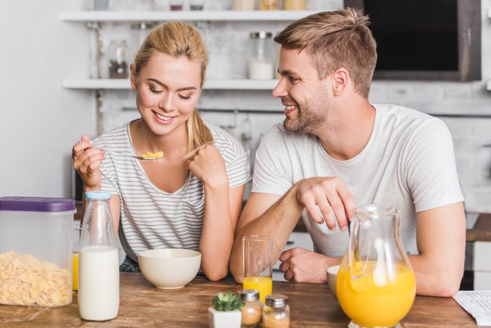 couple having breakfast and eating corn flakes with milk in kitchen